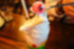 Whipped cream-topped dessert with a fake but edible eyeball on a spoon, set on a wooden table. Bright, colorful layers create a playful mood.
