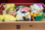 Bento box with sushi, rice, and assorted colorful ingredients, including salmon and tamago, in a red tray. Vibrant and appetizing.