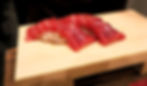 Slices of red tuna sashimi on rice, neatly arranged on a wooden plank, creating an appetizing, vibrant display against a dark background.