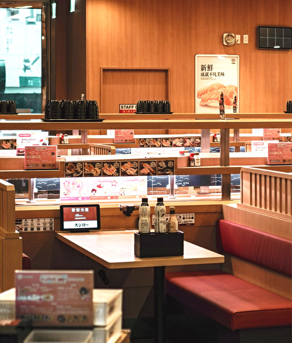 Sushiro conveyor belt sushi restaurant in Tokyo: red seating, and conveyor belt; menus display sushi images; soy sauce bottles on table.
