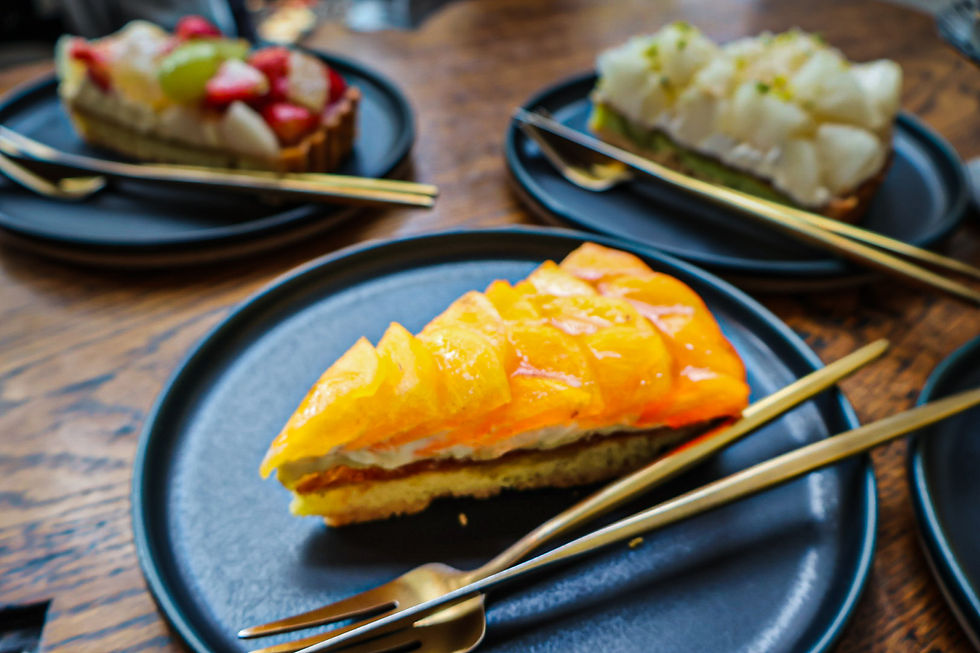 Slices of fruit tarts with vibrant toppings on black plates and gold flatware, set on a wooden table.