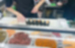 Hands preparing onigiri behind the counter, with rolls lined up on a counter.