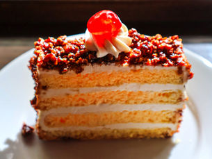 A slice of cake topped with chocolate, whipped cream, and a cherry on a white plate from Ghibli Park