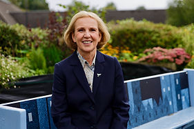 Susan in navy blazer sitting by a decorative garden bench.