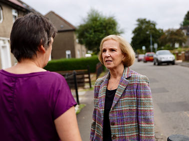 Susan in a tweed jacket talking to another women on the street.