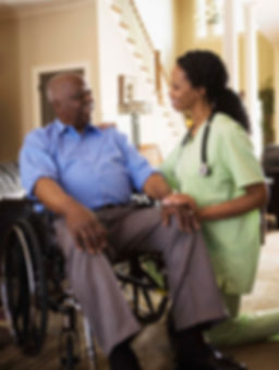A caretaker interacting with an elderly man in a wheelchair in his home