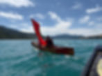Open canoe coaching session using a sail on a blue lake