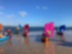 Open canoe coaching with colorful sails on a beach.