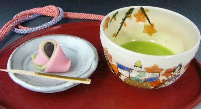 お雛様の絵付けの抹茶茶碗と抹茶、ピンクの和菓子の小皿を赤い盆に置いた桃の節句のお茶