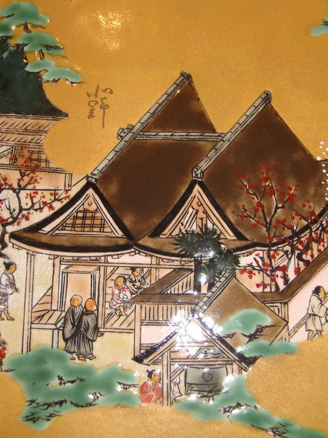 梅や桜の咲く境内に社殿が並ぶ様子を描いた、金色の地の色絵皿