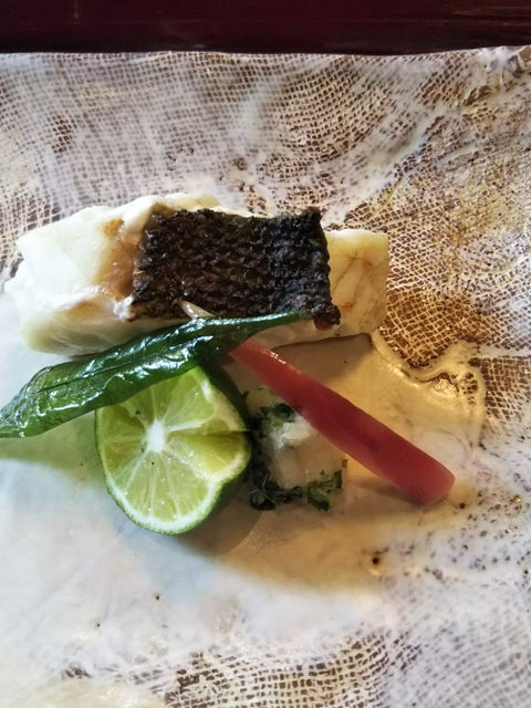 白い焼物の角皿に、皮付きの魚の焼物とすだちを盛り付けた一皿