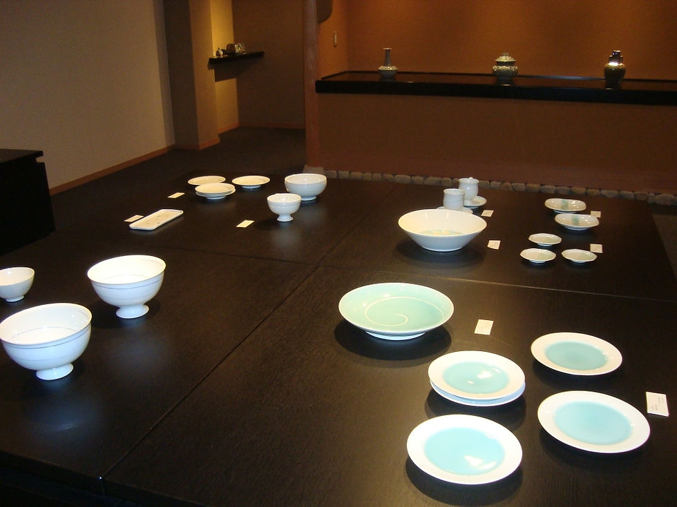黒い展示台に白磁の鉢と、青緑の釉薬が溜まった丸皿を並べた様子