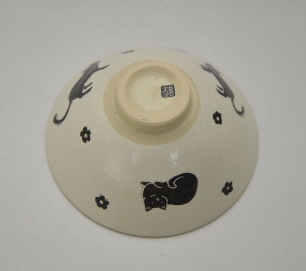 ねこ飯茶碗を伏せて高台を見せた様子。外側に黒猫の絵が回り、高台に作家の印がある