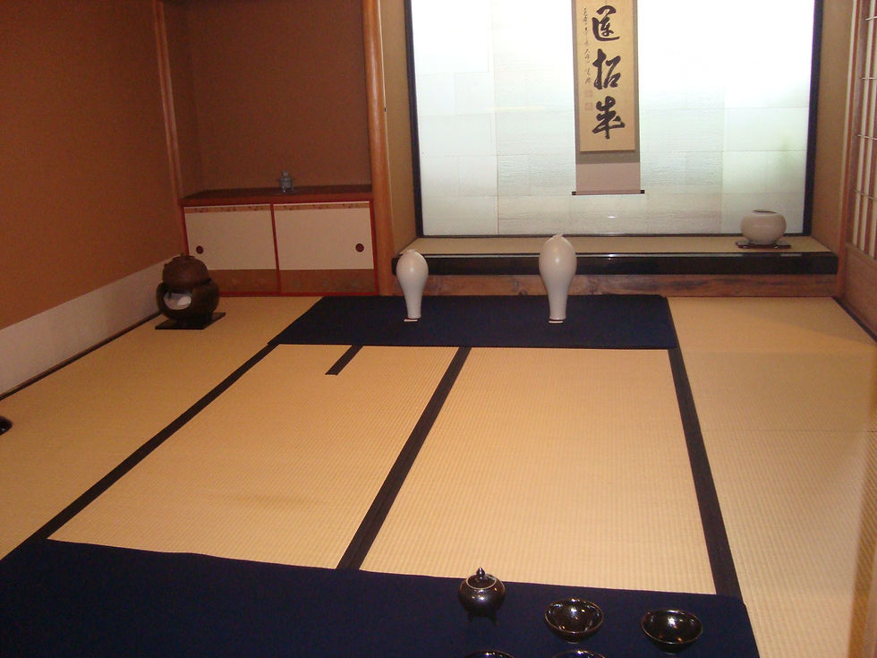 畳敷きの和室。床の間に掛軸と白い花入、手前に黒い茶碗などを置いた展示