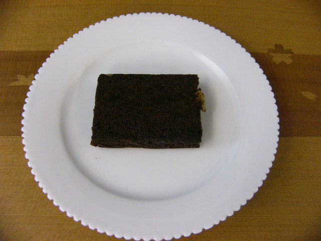 縁飾りのある白い皿に乗せた、四角いチョコレートケーキ