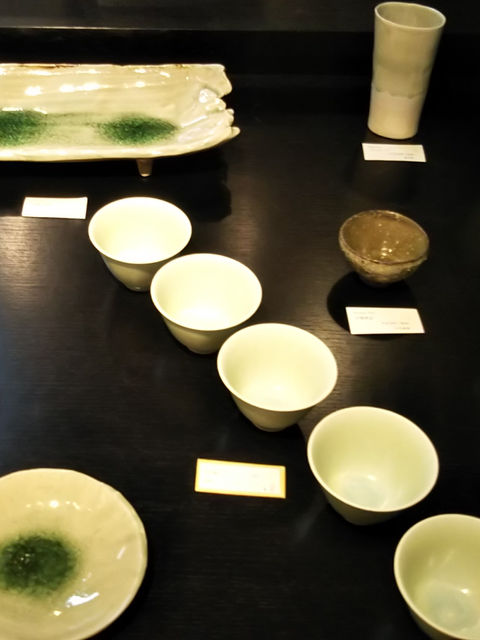 淡い黄緑の釉薬に緑の溜まりがある皿と湯呑を並べた展示