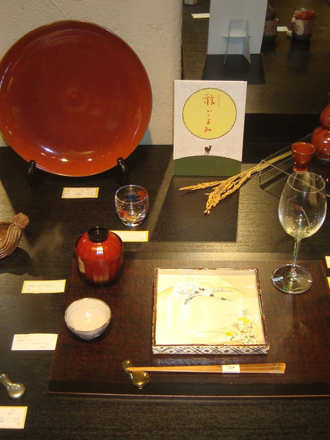 「稲ごよみ」の札と稲穂、朱塗りの大皿やグラスを並べた秋の展示台