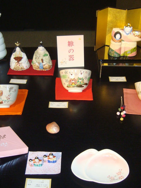「雛の器」の札とお雛様の茶碗、金屏風の前の雛人形、桜柄の皿を並べた展示