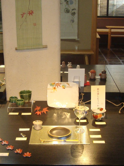 紅葉の枝を添え、緑や赤の器と盃を黒い台に並べた秋の展示