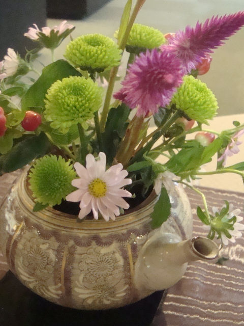 ポットに、ピンクや緑の菊、赤い実、小さな花を生けたテーブルの花