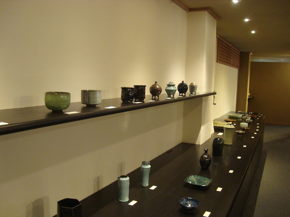壁際の棚と台に茶盌や花入が並ぶ展示室