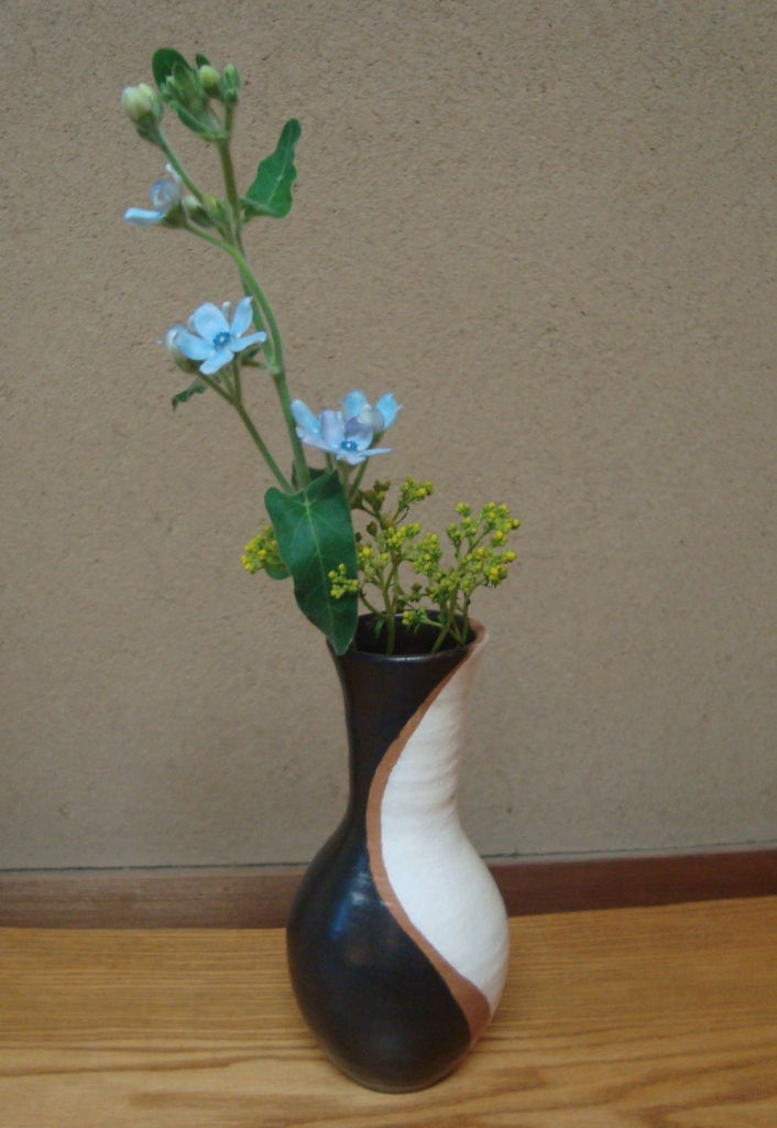 黒と白の花生に、水色の小花と黄色い花を生けた様子