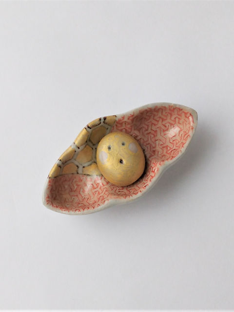 亀甲と赤い麻の葉模様を描いた葉形の豆皿に、黄色い丸い置物をのせたセット