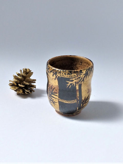 竹の絵を金彩で描いた黒い湯呑、横に金色の松ぼっくり