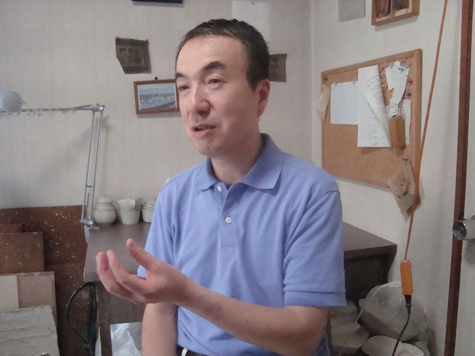 工房で身振りを交えて話をする、水色のポロシャツ姿の西岡義弘さん