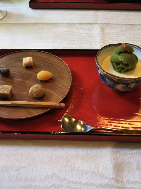 朱塗りの盆に抹茶アイスの器と、小さな和菓子を並べた木の丸皿