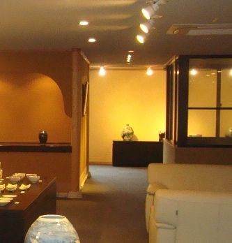 照明の暖かいギャラリー2階の奥の部屋。白いソファと壺が置かれている