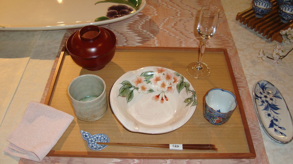 盆の上に朱の蓋付き椀、花の絵皿、湯呑、箸置きを並べた、ランチ会の席の一人分