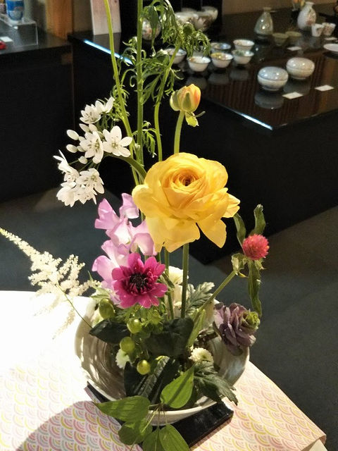 春のテーブルに飾った花。黄色いラナンキュラスやピンクの花を鉢に生けた様子