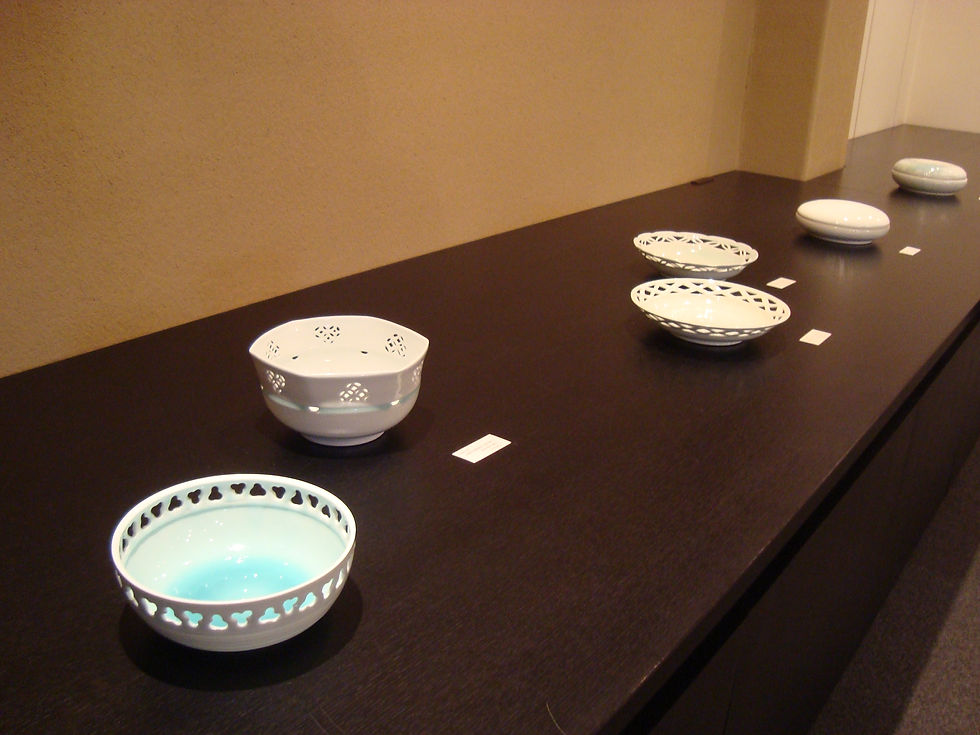 透かし彫りの入った白磁と水色の鉢・皿を長い黒台に並べた展示