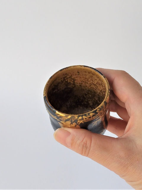 手に持って内側を見せた、金彩と茶色の釉が混ざる竹絵の湯呑