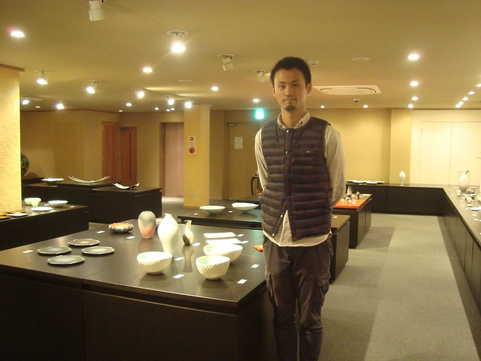 三人展の会場で、器を並べた展示台の前に立つ村田匠也さん