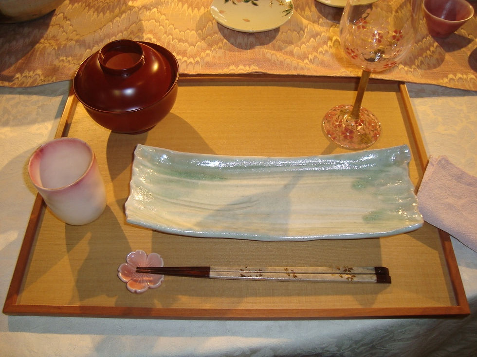 朱色の蓋付き椀と淡緑の長皿、桜柄の箸置きを盆にのせた春の席の様子