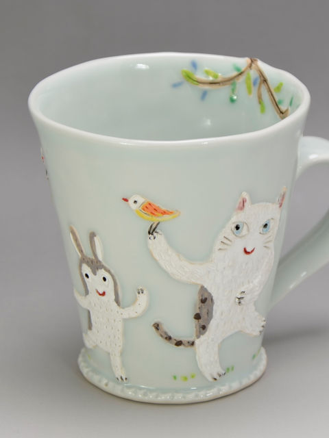 淡い青磁色の地に、小鳥を手にのせた猫とうさぎが立体的に描かれた光玉さんのマグ