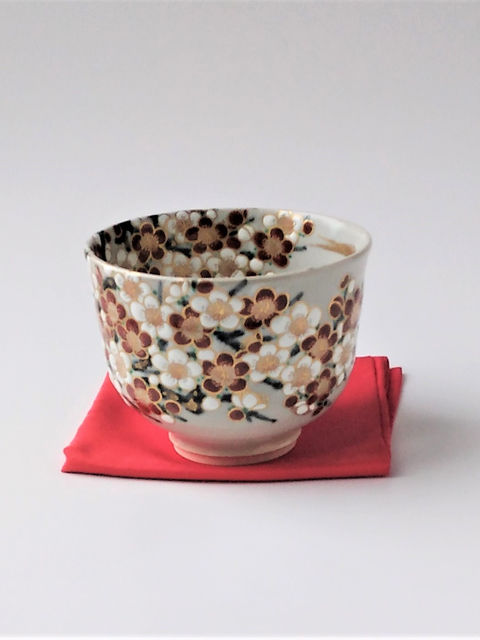赤と白の梅の花が全面に描かれた茶碗、赤い布の上に置いて