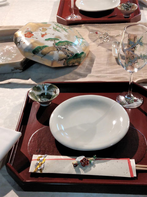 松の絵の蓋物と角鉢、赤い盆の白い皿を並べたお正月の食卓のアップ