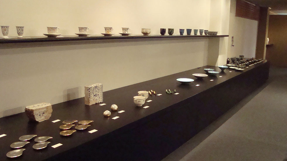 壁の棚と長い黒台に、湯呑・小皿・香合などが整然と並ぶ展示