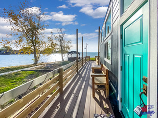 Wanderlust Tiny Home by Indigo River Tiny Homes located at Peninsula Point RV & Tiny Home Resort. View of the front door of the home with the deck leading to the lake..