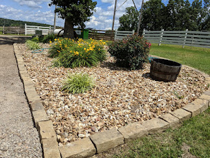 Decorative river rock planter bed with natural stone edging, yellow flowers, shrubs, and a small ornamental tree.