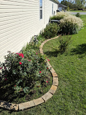 Curved stone landscape edging with flowering shrubs and ornamental grasses along home foundation.
