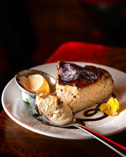 Moody photo, featuring a Basque cheesecake, with a spoonful of cheesecake and ice cream. garnished with flowers.