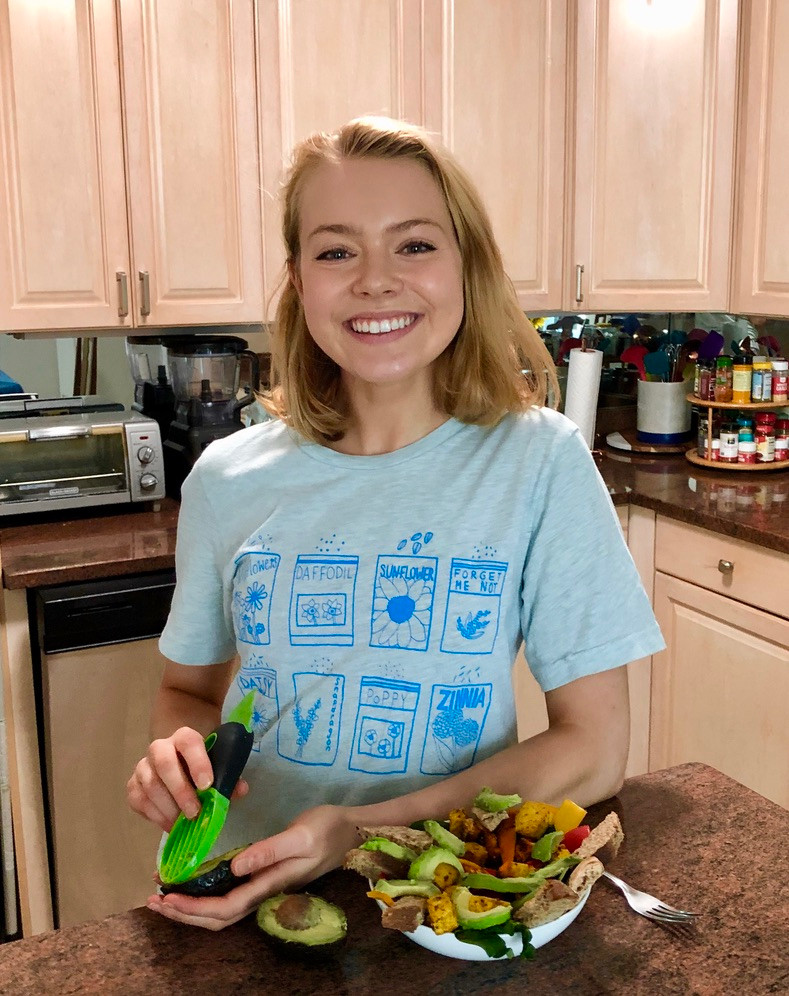 Andrea slicing an avocado with her toast bowl prepared, smiling in her kitchen.