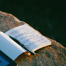 Notebook, pen, e-reader on rock among la