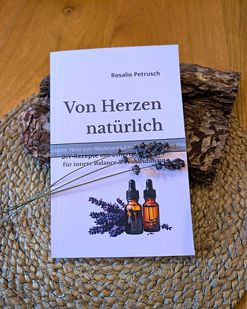 Das Buch ‚Von Herzen natürlich‘ liegt auf einem Stück Baumrinde und einem runden Tischset aus Bast, darüber ein Lavendelzweig – natürliche, ruhige Buchszene.