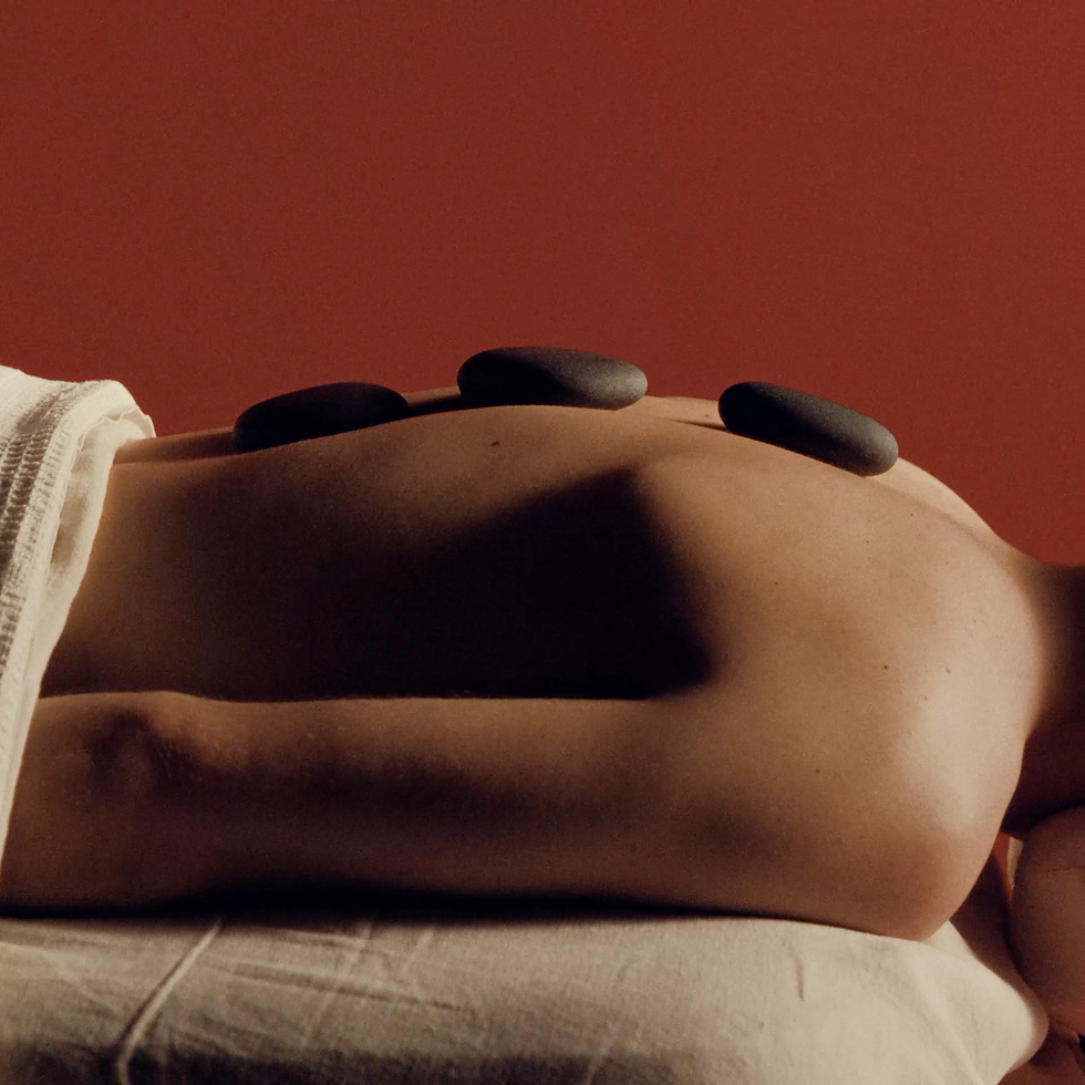 Black hot stones rest on a person's bare back during a massage against a warm red wall.