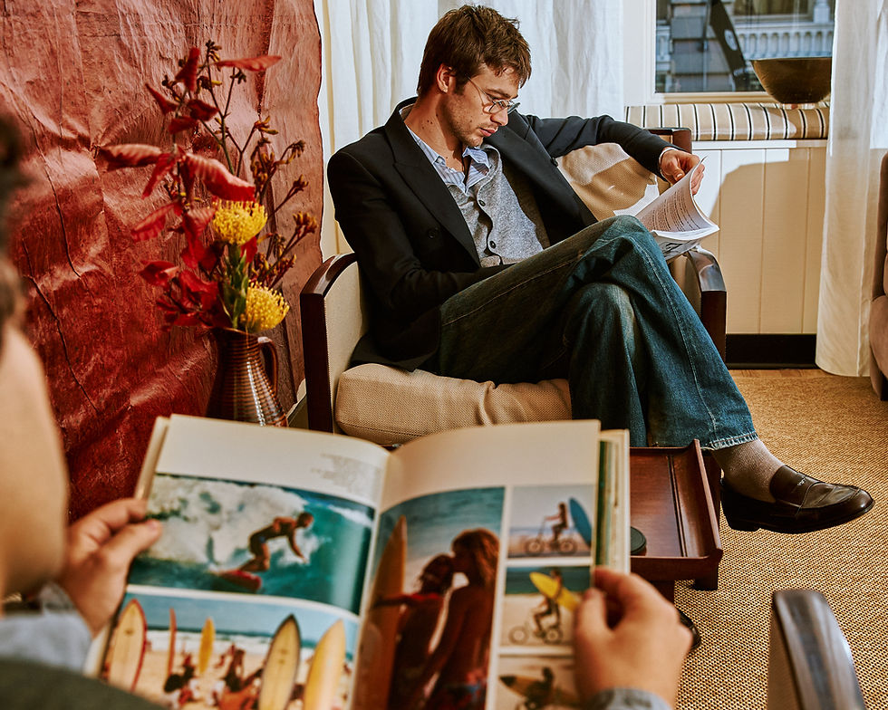 Man in blazer reads papers in spencer's lounge while another person studies a magazine in the foreground
